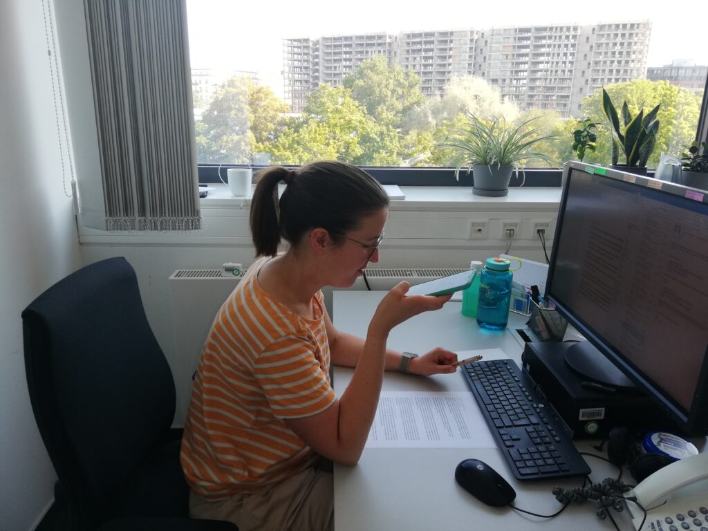 Claudia Wöckel sitzt am Schreibtisch und hält ihr Smartphone in der Hand