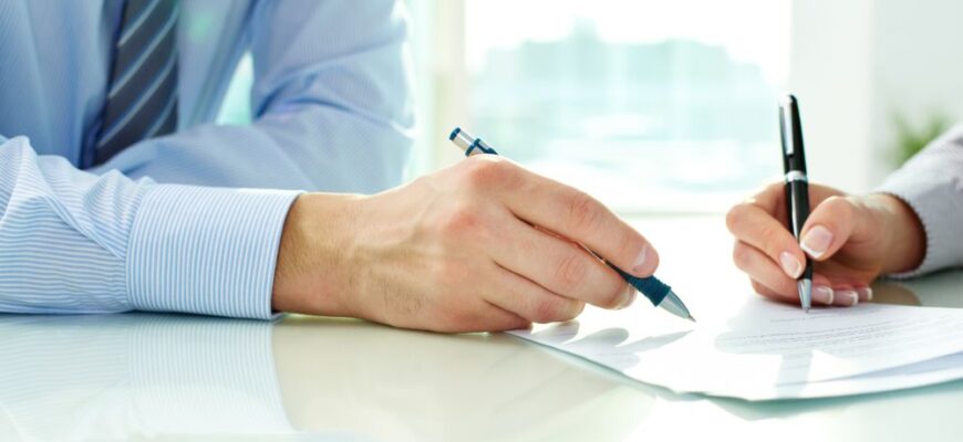 zwei Hände mit Stiften in der Hand, die ein Dokument unterzeichnen