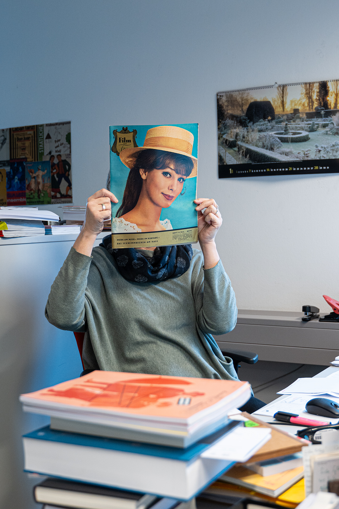 In einem Büro hält sich eine Person eine Ausgabe der Zeitschrift "Film und Frau" vor das Gesicht. Es sieht aus, als wäre der Kopf der Frau auf dem Magazincover der Kopf der Person im Büro.