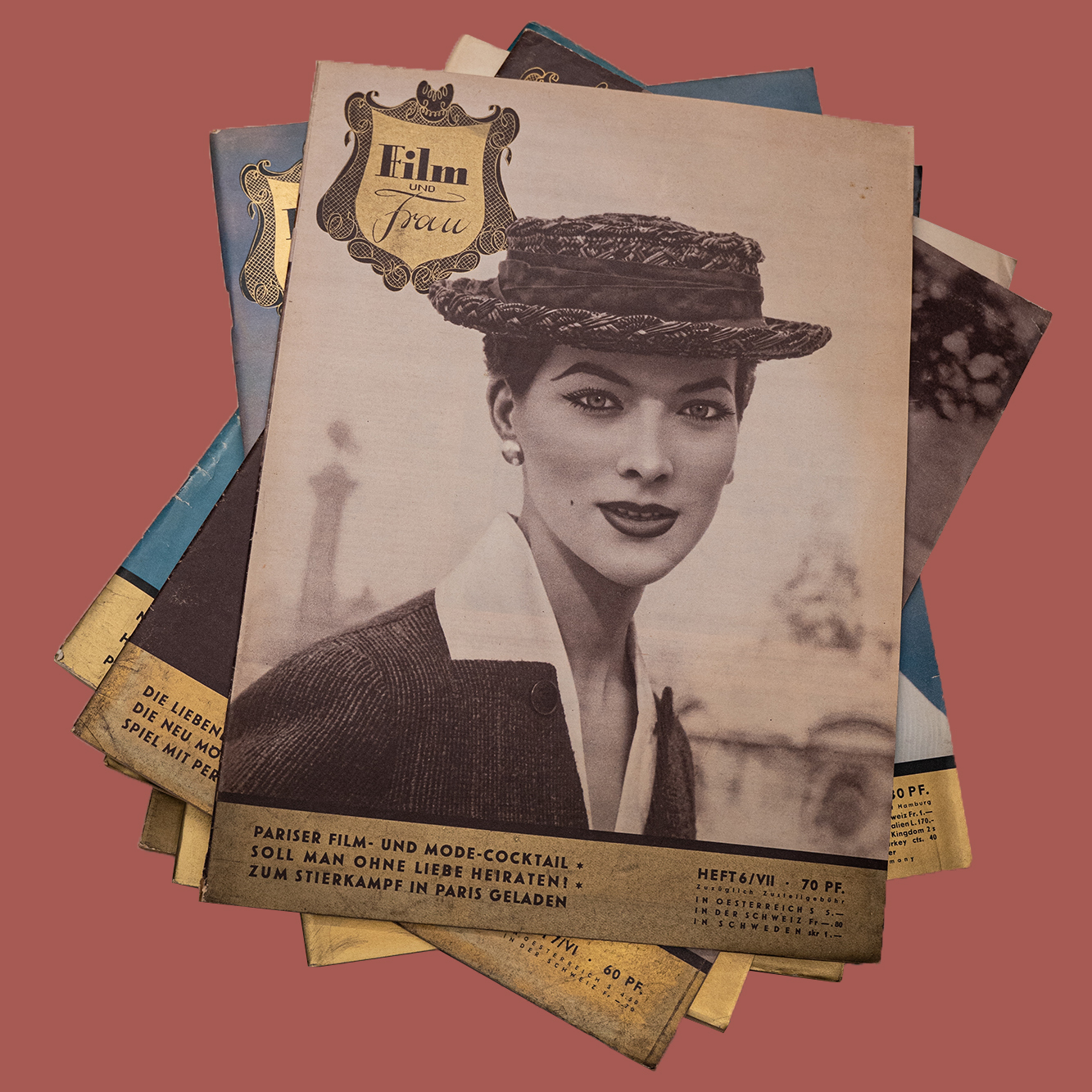 Mehrere Zeitschriften liegen auf einem Stapel auf einer roten Unterlage. Auf dem Coder ist eine schwarz-weiß Fotografie einer Frau zu sehen.
